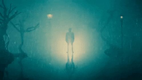 a man is standing in the rain in a dark forest
