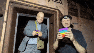 a man in a suit and a man in a hat holding a rainbow pop it