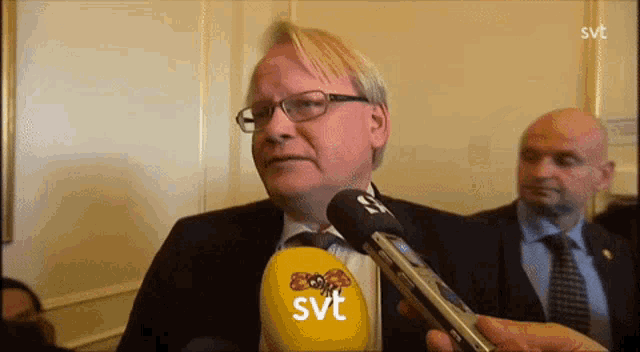 a man wearing glasses is being interviewed by a yellow svt microphone