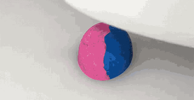 a pink and blue ball sitting on a white surface