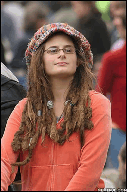 a woman with dreadlocks and glasses is wearing a hat and a red jacket