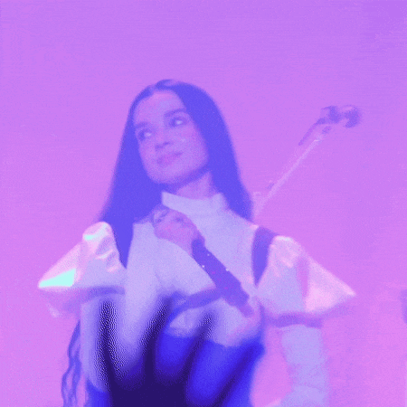 a woman in a white shirt is holding a microphone in front of a purple background