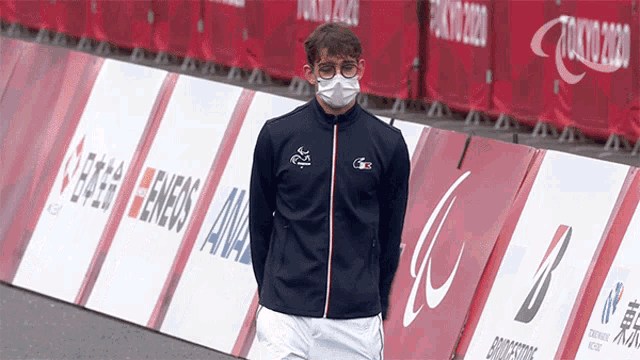 a man wearing a face mask stands in front of a tokyo 2020 banner