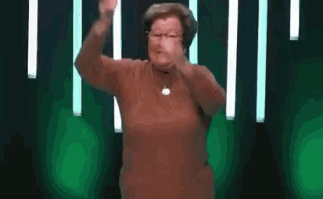 a woman in a brown sweater is standing in front of a green background and making a funny face .