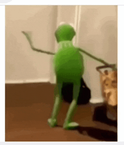 a green kermit the frog is dancing on a wooden floor .