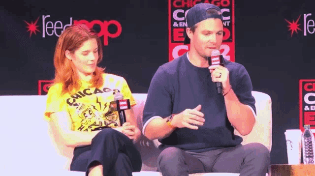 a man is talking into a microphone while a woman sits behind him
