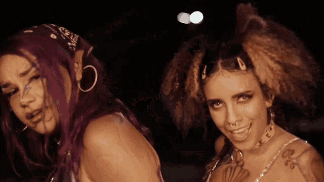 a woman with purple hair and a bandana on her head stands next to another woman