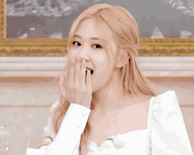 a woman covering her mouth with her hand while wearing a white top