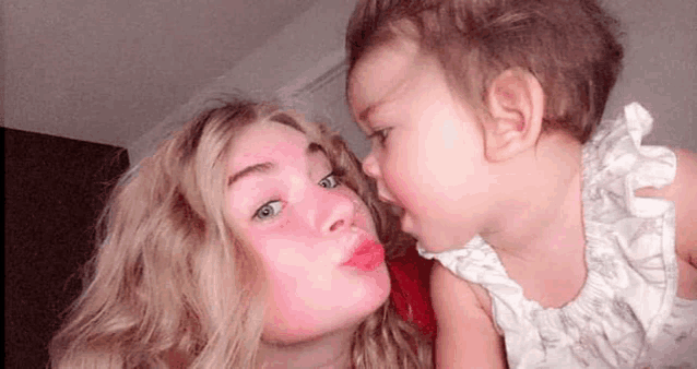 a woman is holding a baby in her arms and kissing it on the cheek .