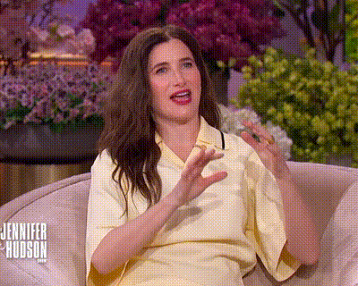 a woman in a yellow shirt is sitting on a couch with her hands out .