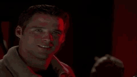 a man is standing in a dark room with a red light behind him .