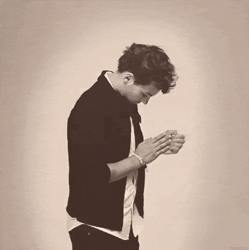 a man in a black jacket and white shirt is praying with his hands together .
