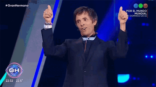 a man in a suit is giving a thumbs up in front of a sign that says gran hermano