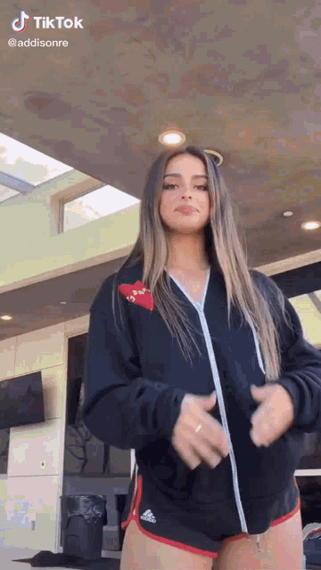 a woman in a black hoodie and red shorts is standing in front of a building .