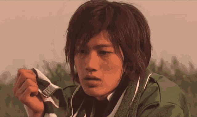 a young man in a green jacket holds a piece of cloth