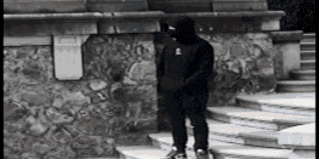 a man in a black hoodie is standing on a set of stairs .