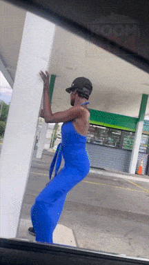a man in a blue dress is leaning against a pole in front of a gas station