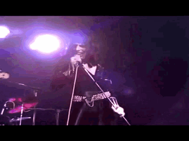 a woman is singing into a microphone while holding a guitar on a stage .