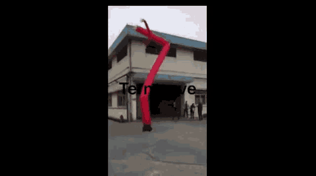 a red inflatable clown is flying through the air in front of a building .