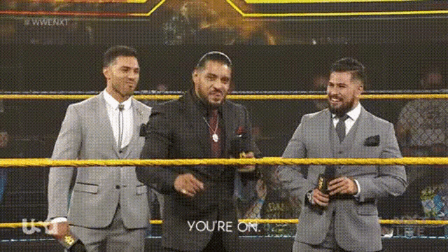 three men in suits are standing in a wrestling ring and one of them is saying you 're on