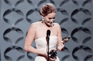 a woman in a white dress is standing in front of a microphone holding an oscar .