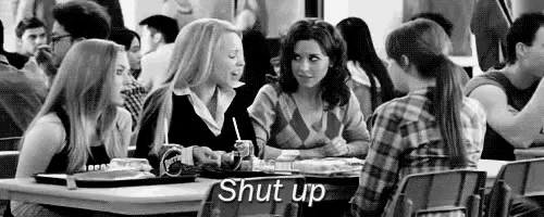 a group of girls are sitting at a table in a cafeteria talking to each other .