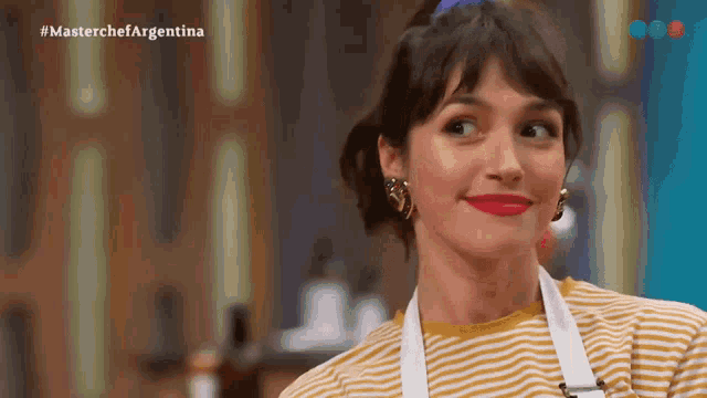 a woman wearing a yellow and white striped shirt and an apron is smiling