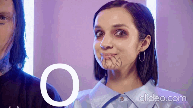 a woman with a tattoo on her face looks at the camera with the letter o in the background
