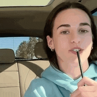 a woman is sitting in the back seat of a car holding a pen in her mouth .