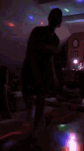 a silhouette of a person dancing in a dark room with colorful lights
