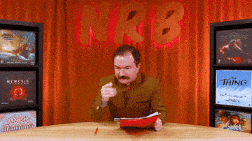 a man sitting at a table in front of a sign reading nrb