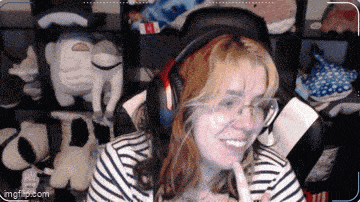 a woman wearing headphones and glasses is smiling in front of a shelf of stuffed animals