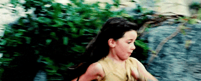 a young girl is running across a river in a forest .