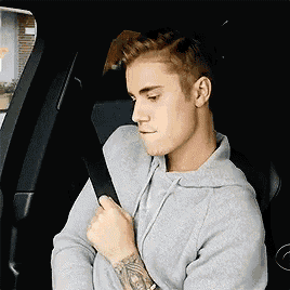 justin bieber is sitting in a car holding a seat belt .