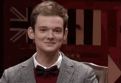 a young man wearing a suit and bow tie is smiling in front of a british flag .