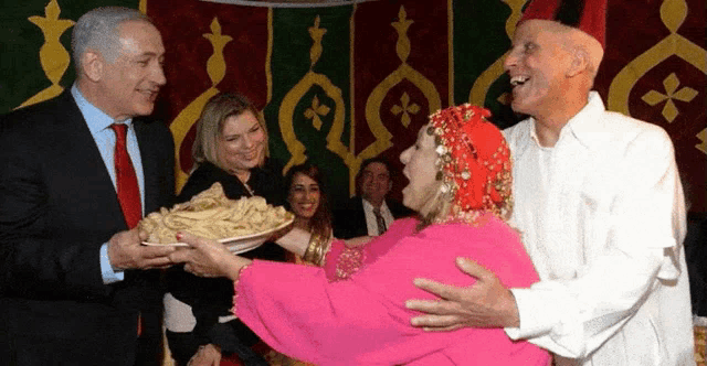a man in a suit and tie holds a plate of food in front of a woman in a pink dress