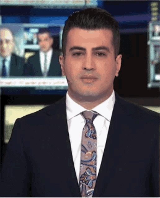 a man in a suit and tie is standing in front of a television screen