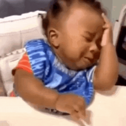 a baby is crying while sitting at a table and holding his head .