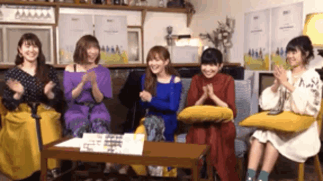 a group of women are sitting around a table clapping