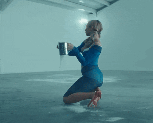 a woman in a blue dress is kneeling down and holding a metal can