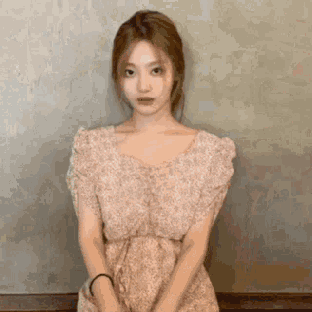 a woman in a floral dress is standing in front of a wall .