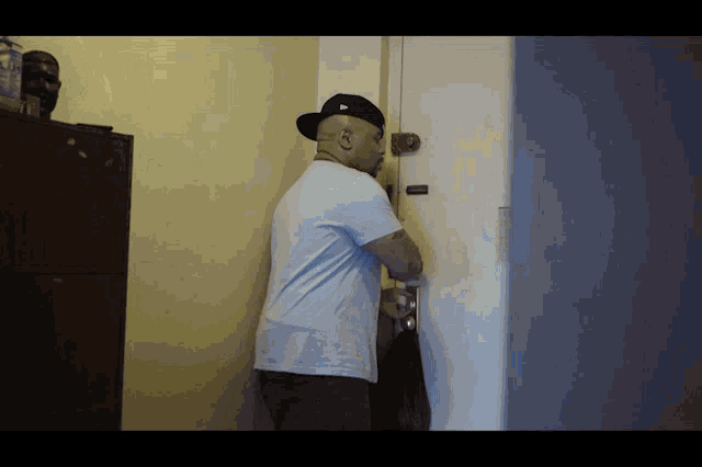 a man wearing a hat and a white shirt is standing in a doorway