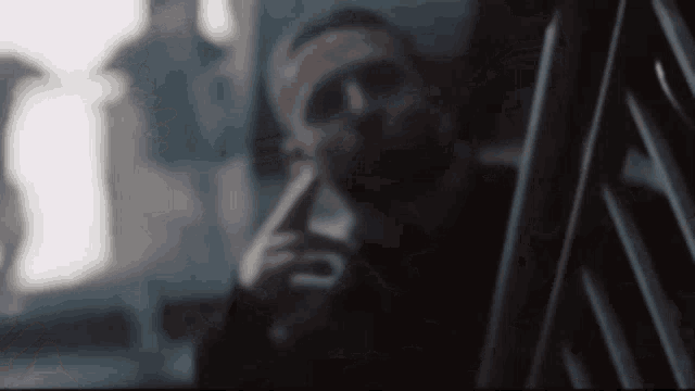 a man with a beard is smoking a cigarette while standing next to a railing .