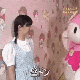 a girl is standing next to a pink hello kitty mascot .