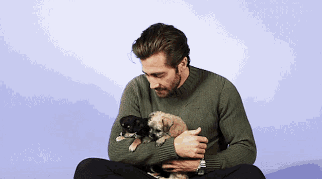 a man in a green sweater holds two puppies