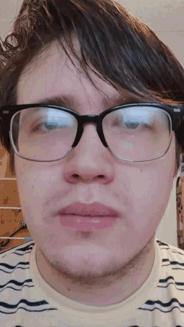 a young man wearing glasses and a striped shirt looks at the camera