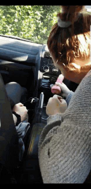 a woman sitting in a car holding a pink object in her hand