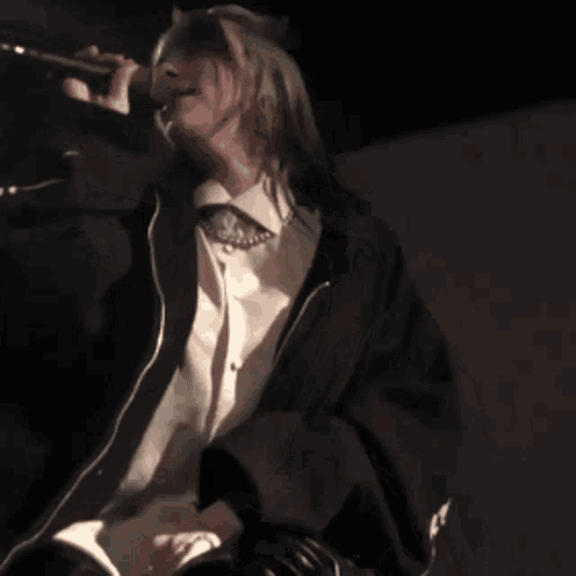 a woman is singing into a microphone while wearing a white shirt and a black jacket