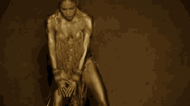 a woman in a gold bodysuit is dancing on a brown background .