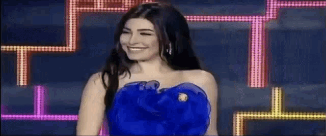 a woman in a blue dress is smiling while standing in front of a maze of lights .